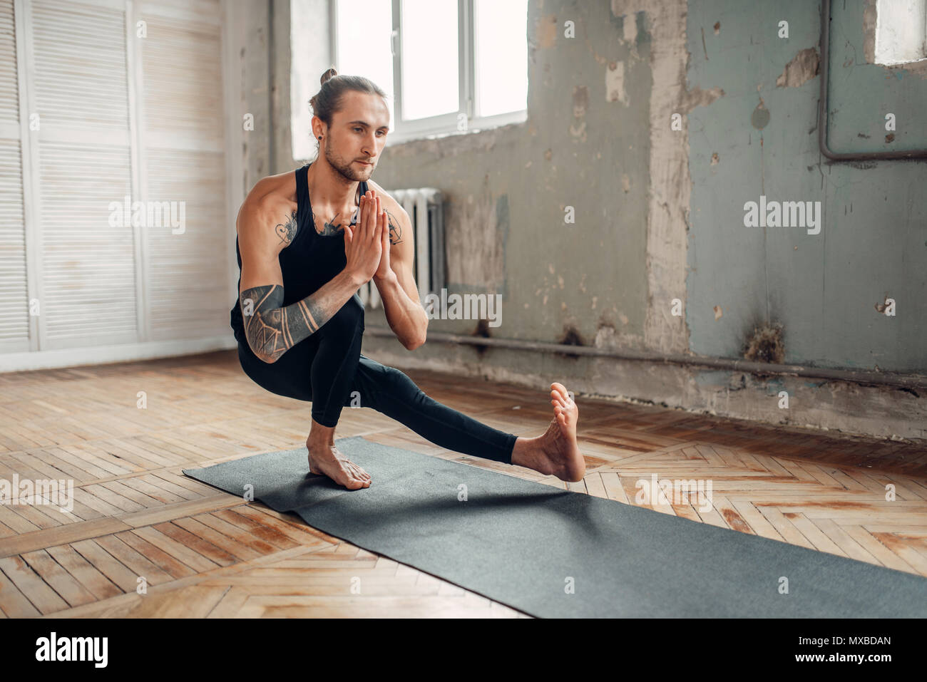 Yoga maschio in classe, l'equilibrio di formazione. Esercizio sul tappeto in palestra con grunge interni. Montare l'allenamento al chiuso Foto Stock