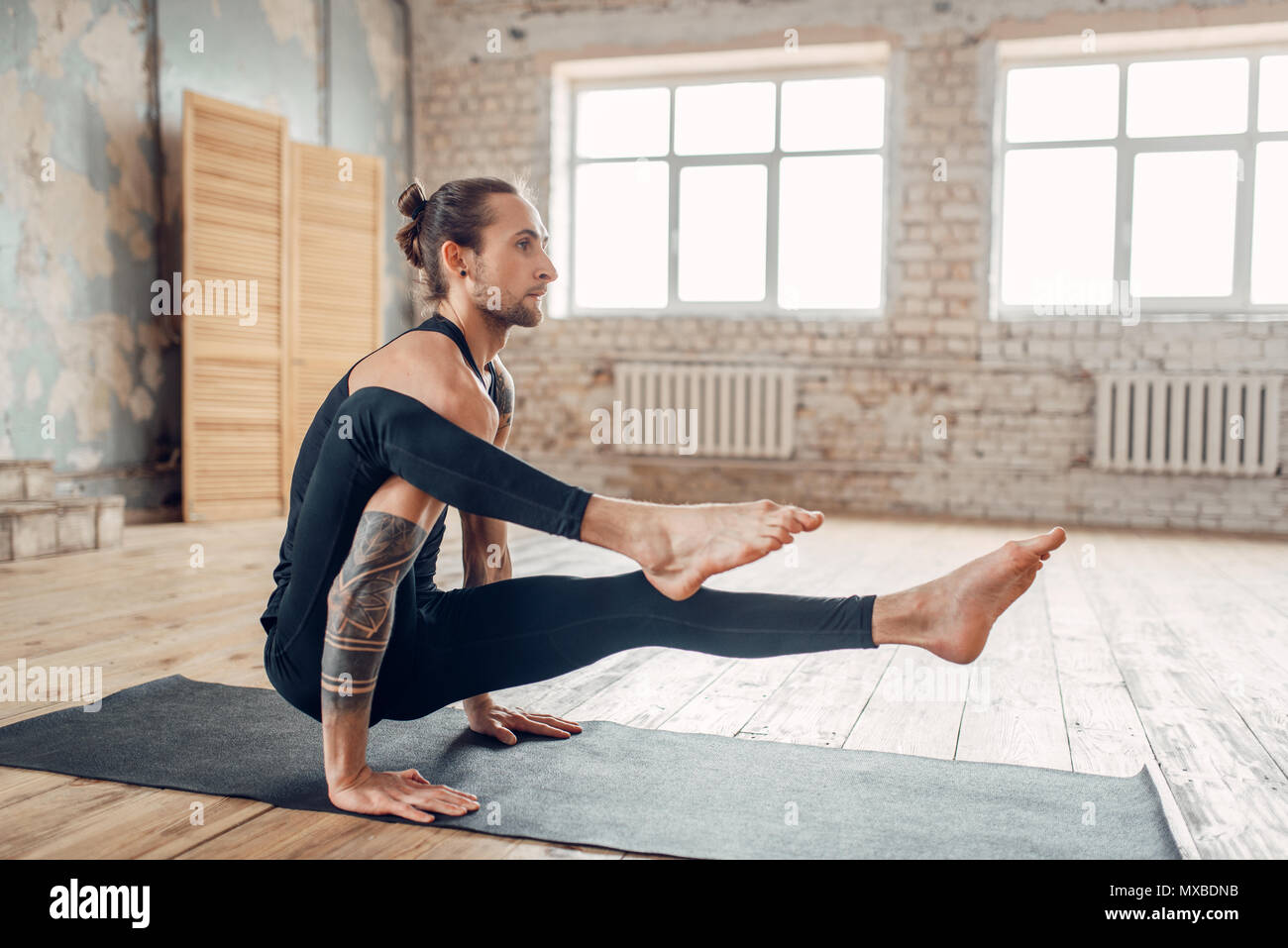 Maschio di yoga in palestra, esercizio di bilanciamento su mat. Allenamento fitness in ambienti chiusi. Uno stile di vita sano Foto Stock