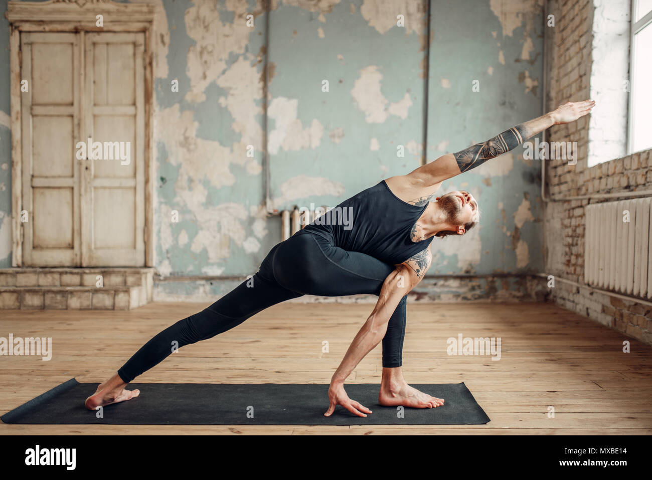 Yoga maschio facendo esercizio di flessibilità sul tappeto in palestra con grunge interni. Montare l'allenamento indoor, yogi studio Foto Stock