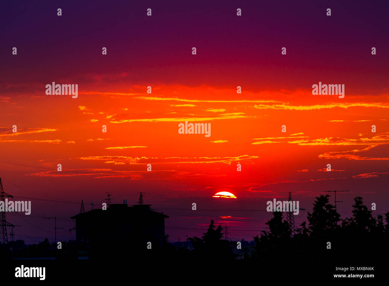 Rosso fuoco tramonto urbano con silhouette nera di pali della luce e delle case di paesaggio. Copia dello spazio. Rosso tramonto sullo sfondo. Foto Stock