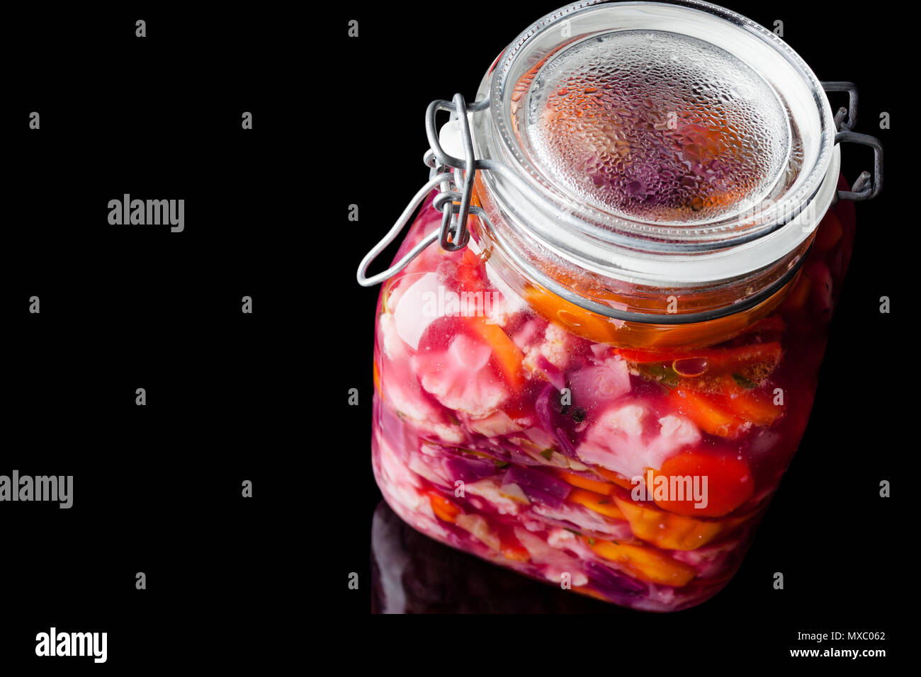 Grande Vaso in vetro colorato con verdure sottaceto su sfondo nero con la riflessione dal di sopra Foto Stock