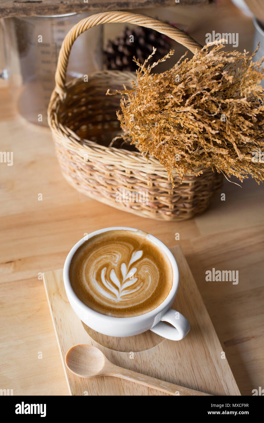 Una tazza di caffè latte con fiori secchi nel cesto su tavola di legno. Foto Stock