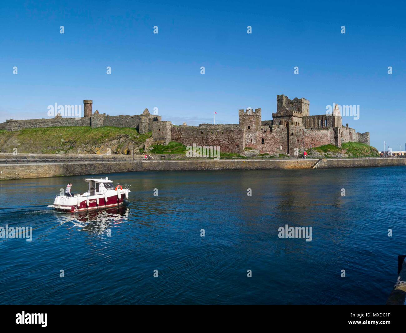 Barca da pesca lasciando Peel Marina passato l'imponente castello di pelatura su San Patrizio Isola Isola di Man sul bel giorno di maggio con cielo blu senza nuvole Foto Stock