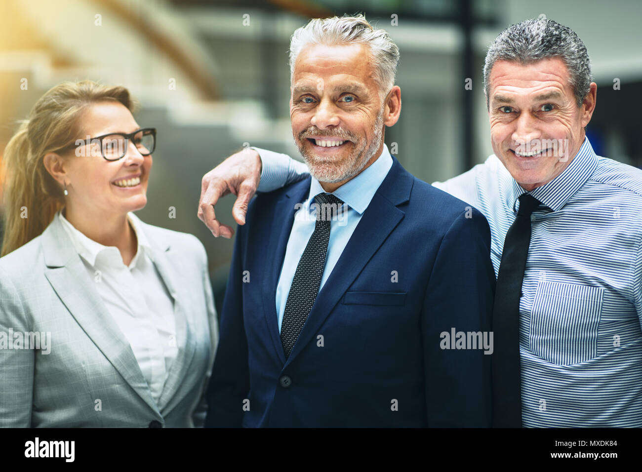 Gruppo sorridente maturo di imprenditori in piedi felicemente insieme nella lobby di un moderno edificio per uffici Foto Stock