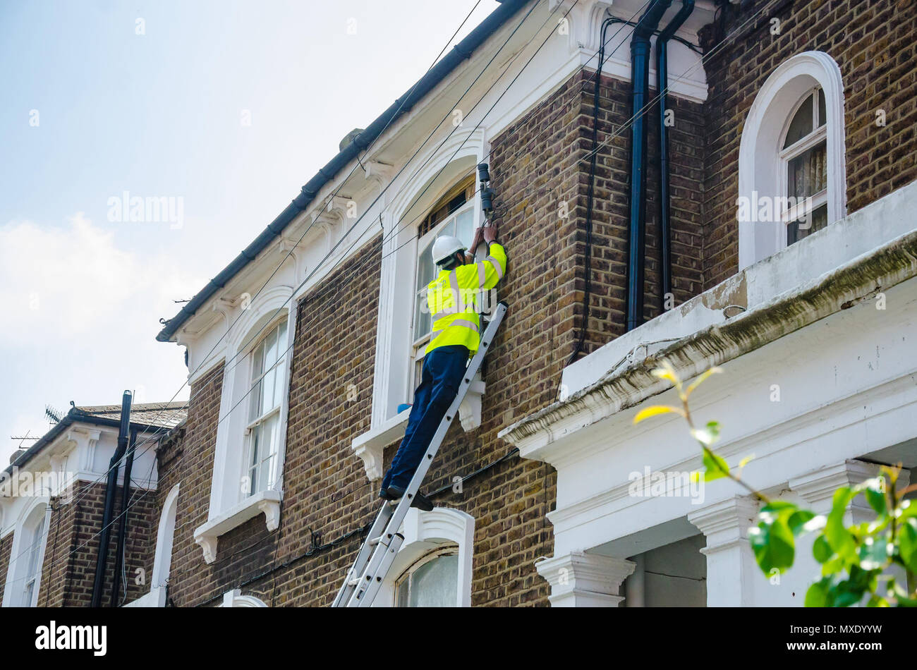 Un ingegnere Openreach su una scala lavorando su una linea telefonica che collega a una proprietà residenziale. Foto Stock