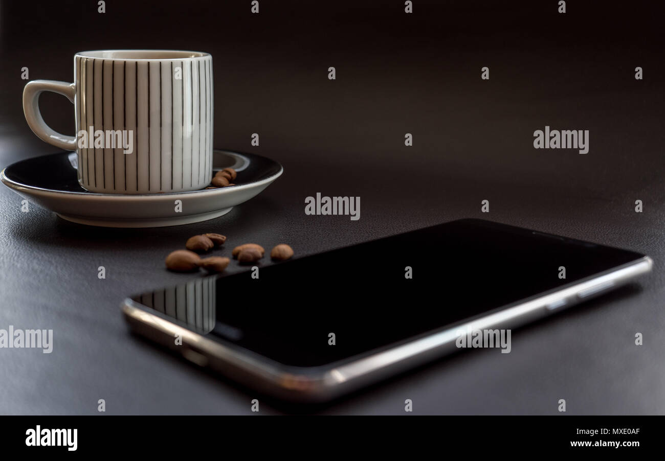 Smartphone oltre al caffè scuro sulla superficie di pelle con i chicchi di caffè Foto Stock