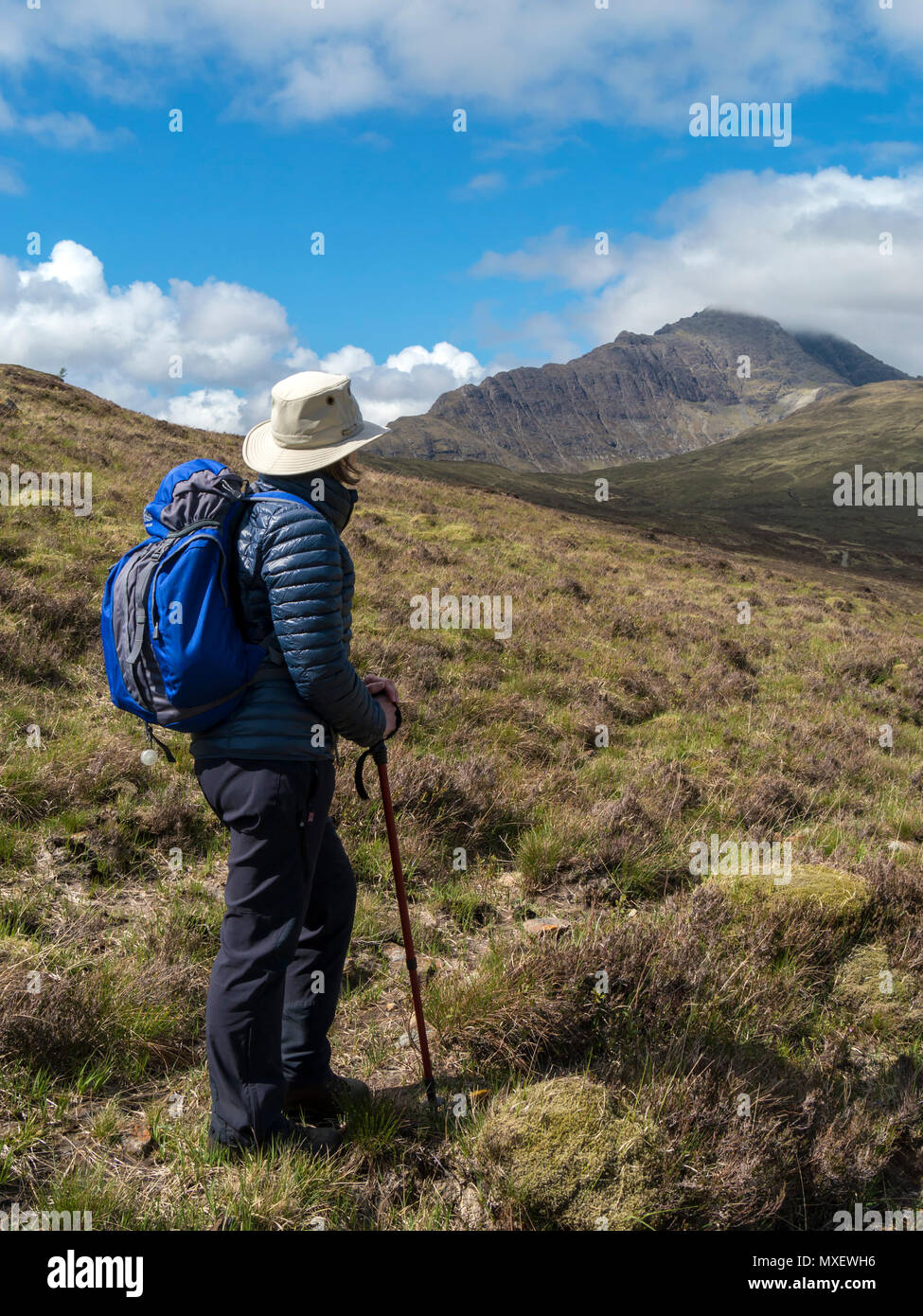 Femmina walker hill con zaino in spalla, walking palo e cappello per il sole con Blaven nel Black Cuillin montagne in distanza, Isola di Skye, Scotland, Regno Unito Foto Stock