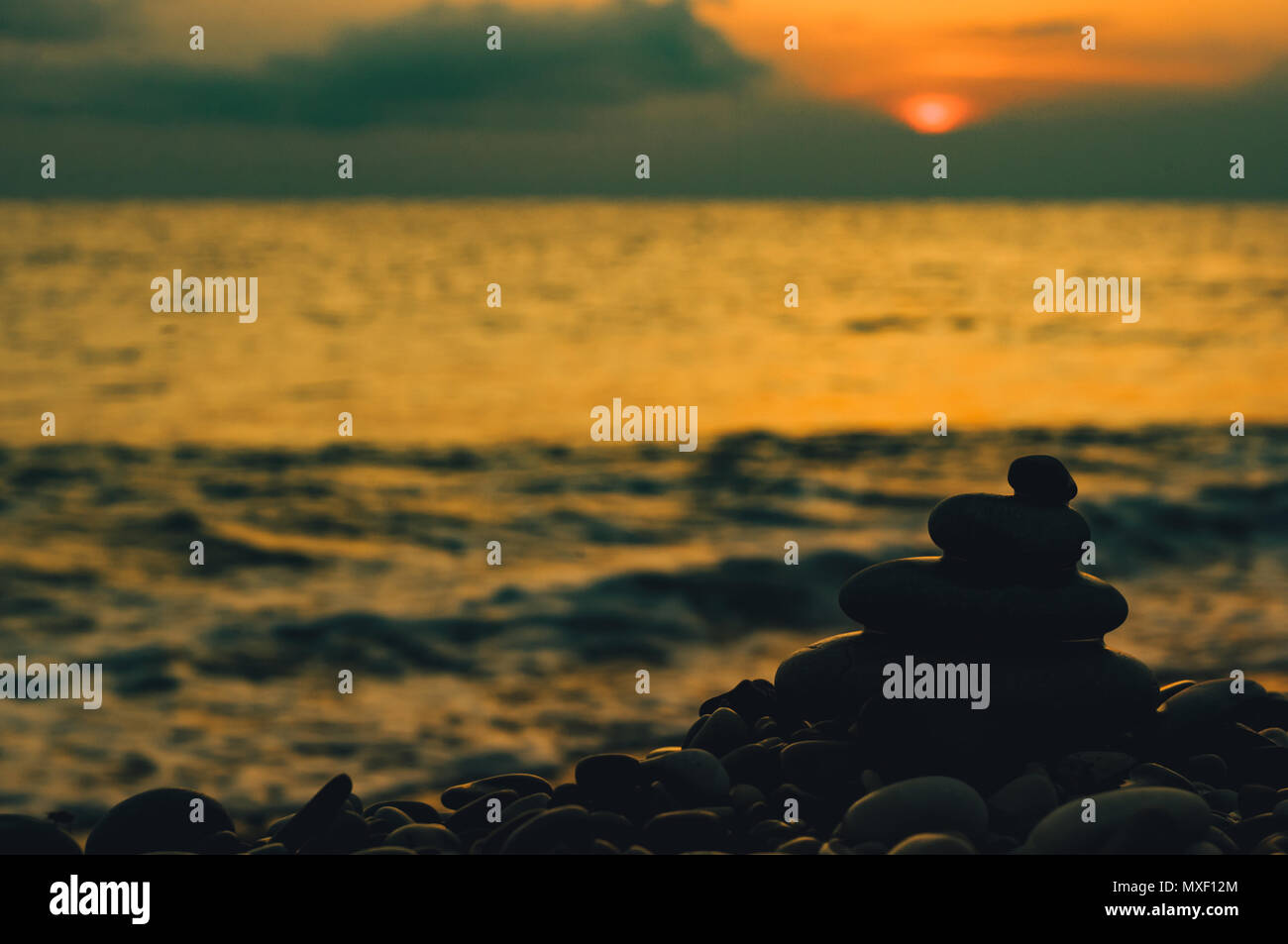 Piramide piegata Zen pietre ghiaia sul mare spiaggia al tramonto Foto Stock