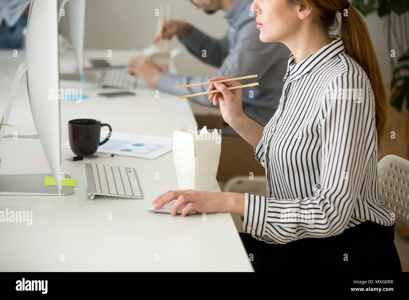 Femmina focalizzata a mangiare cibo asiatico mentre si lavora al computer desktop comput Foto Stock