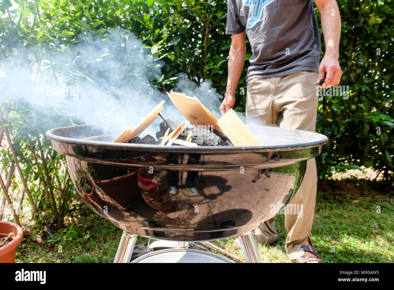 Una giornata di sole in giardino, iniziando il fuoco nel grill e poi cuocere carne con gli amici Foto Stock