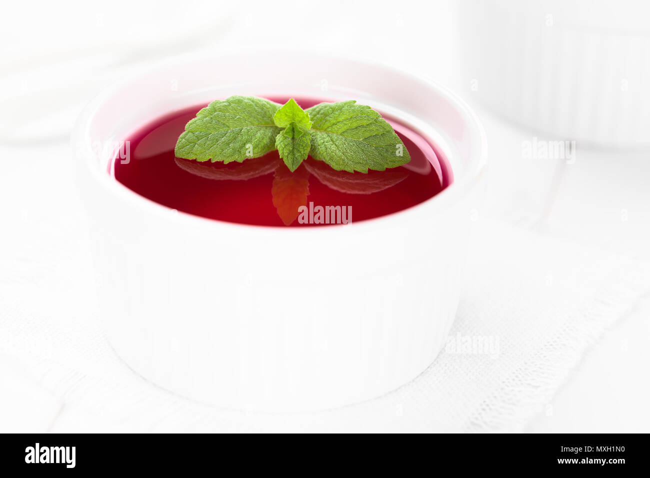 Gelatina rossa o jella nella ciotola bianco guarnito con foglie di menta (messa a fuoco selettiva, concentrarsi sulle punte delle grandi foglie di menta) Foto Stock