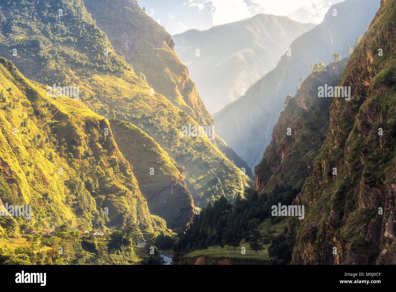 Colorato paesaggio di alta montagna himalayana, foresta verde, cielo blu con nuvole e sole giallo al sorgere del sole in estate in Nepal. La valle di montagna Foto Stock