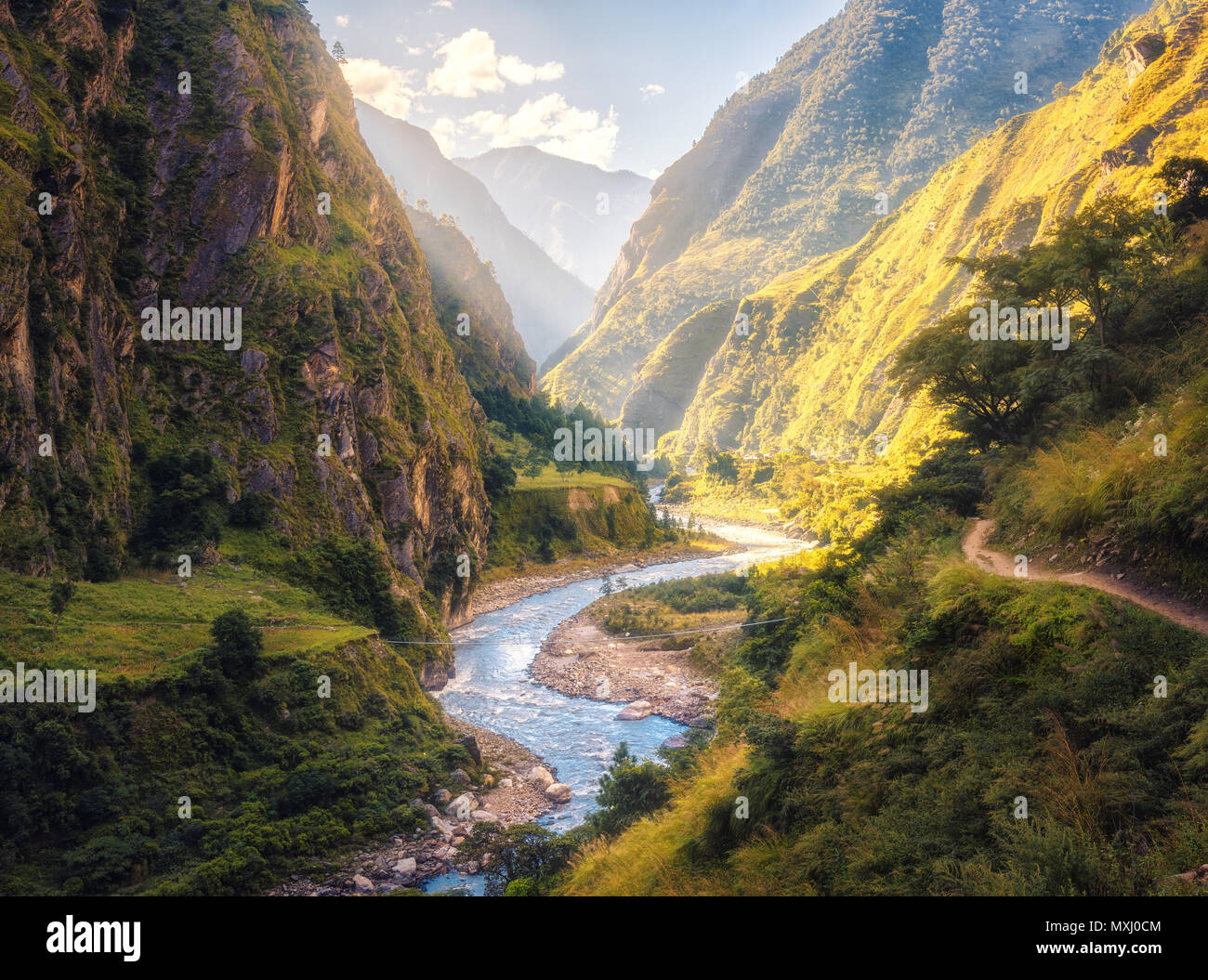 Colorato paesaggio di alta montagna himalayana, bellissimo fiume di curvatura, foresta verde, cielo blu con nuvole e giallo sole al tramonto in estate Foto Stock