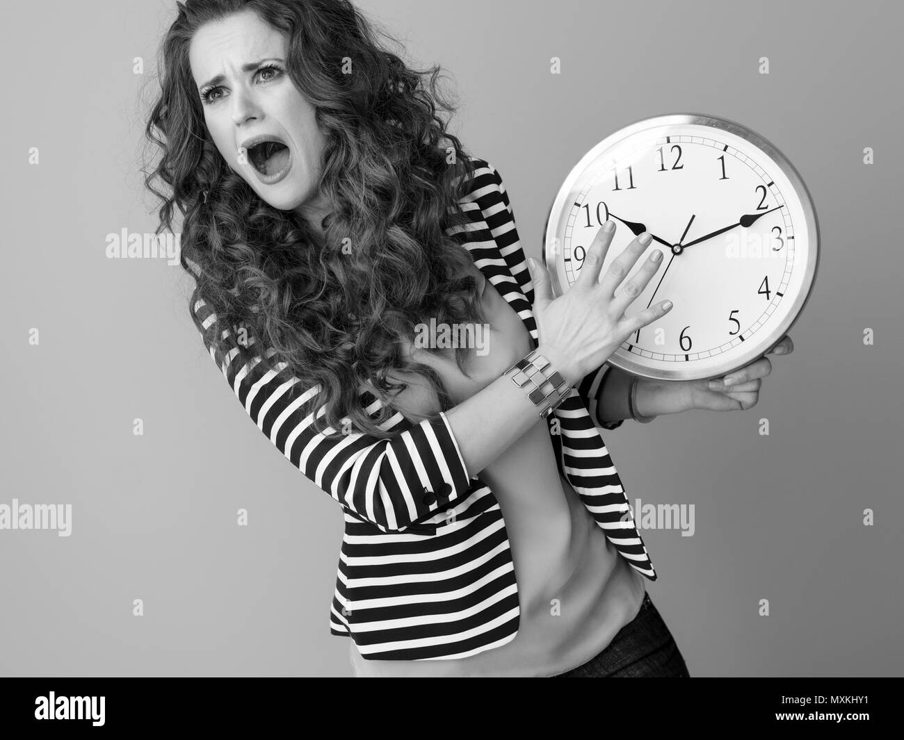 Triste donna elegante in camicia a righe sullo sfondo con orologio Foto Stock