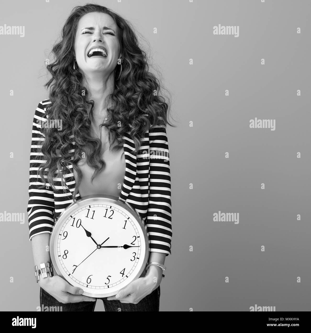 Triste donna elegante con lunga ondulato brunette capelli isolati su sfondo con orologio Foto Stock