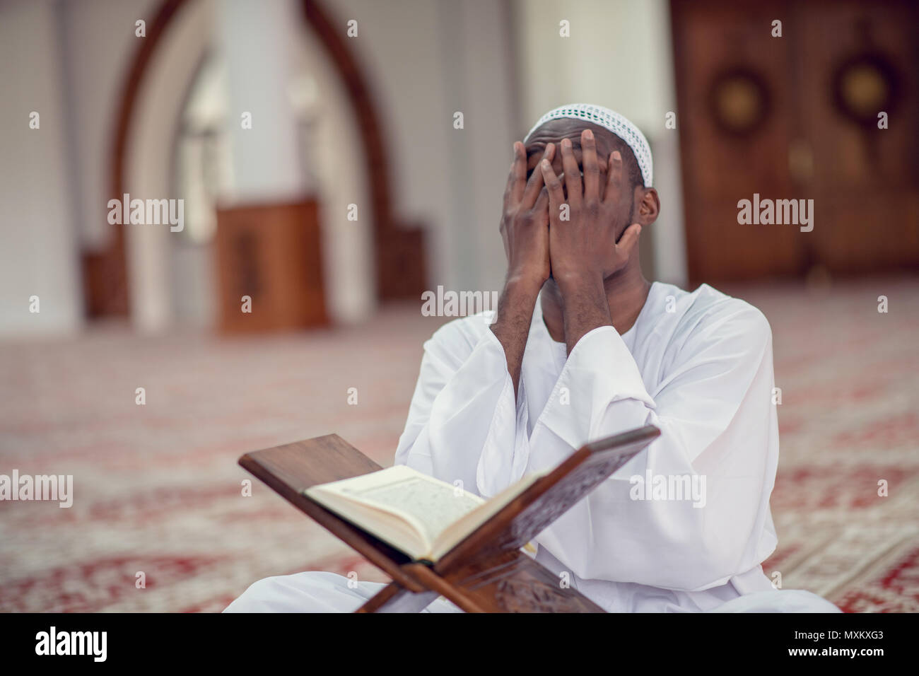 Neri africani uomo musulmano è in preghiera nella moschea di aprire il libro sacro del Corano Foto Stock