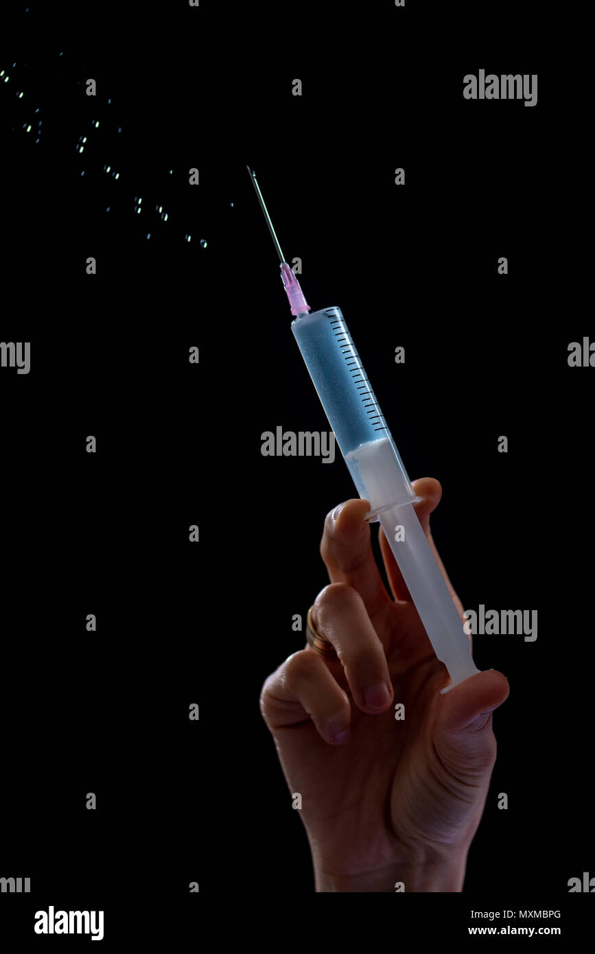 Siringa con una medicina in mani femminili, isolato su nero. Foto Stock