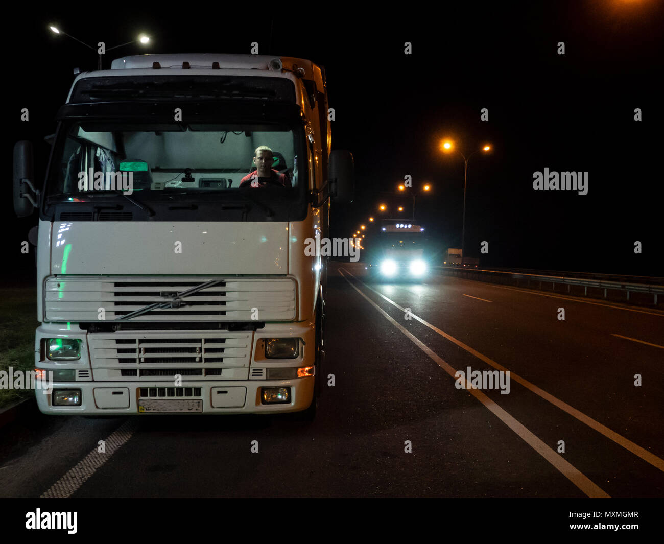 Conducente siede nella cabina di un autocarro parcheggiato sul ciglio della strada di notte Foto Stock