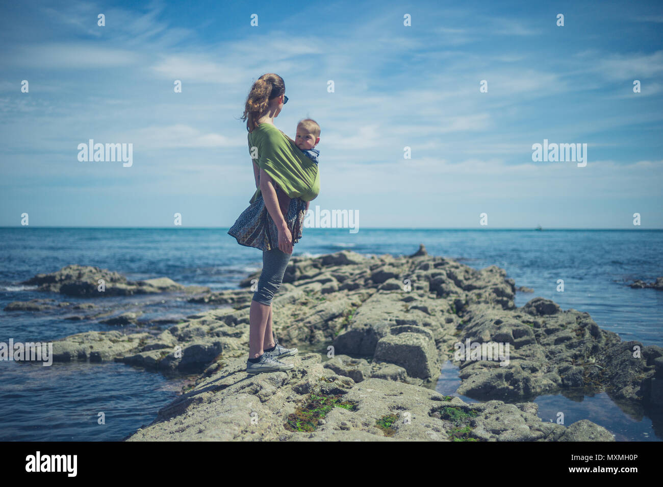 Una giovane madre sta camminando lungo la costa con il suo bambino in una imbracatura Foto Stock