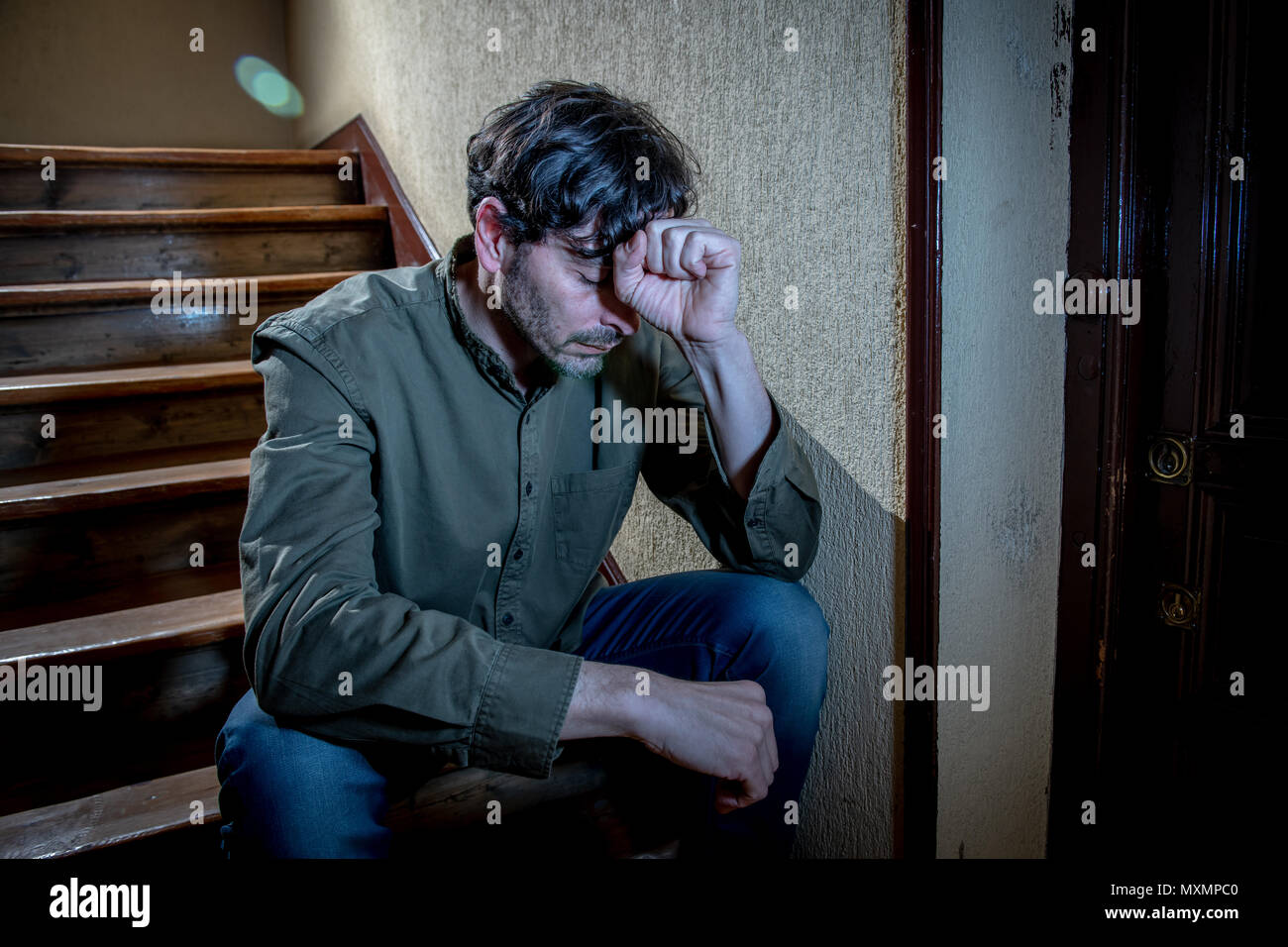 Premuto il latino uomo seduto in testa le mani all'interno di una rampa di scale sentirsi soli e tristi e sottolineato circa il lavoro e la vita in una salute mentale concetto Foto Stock