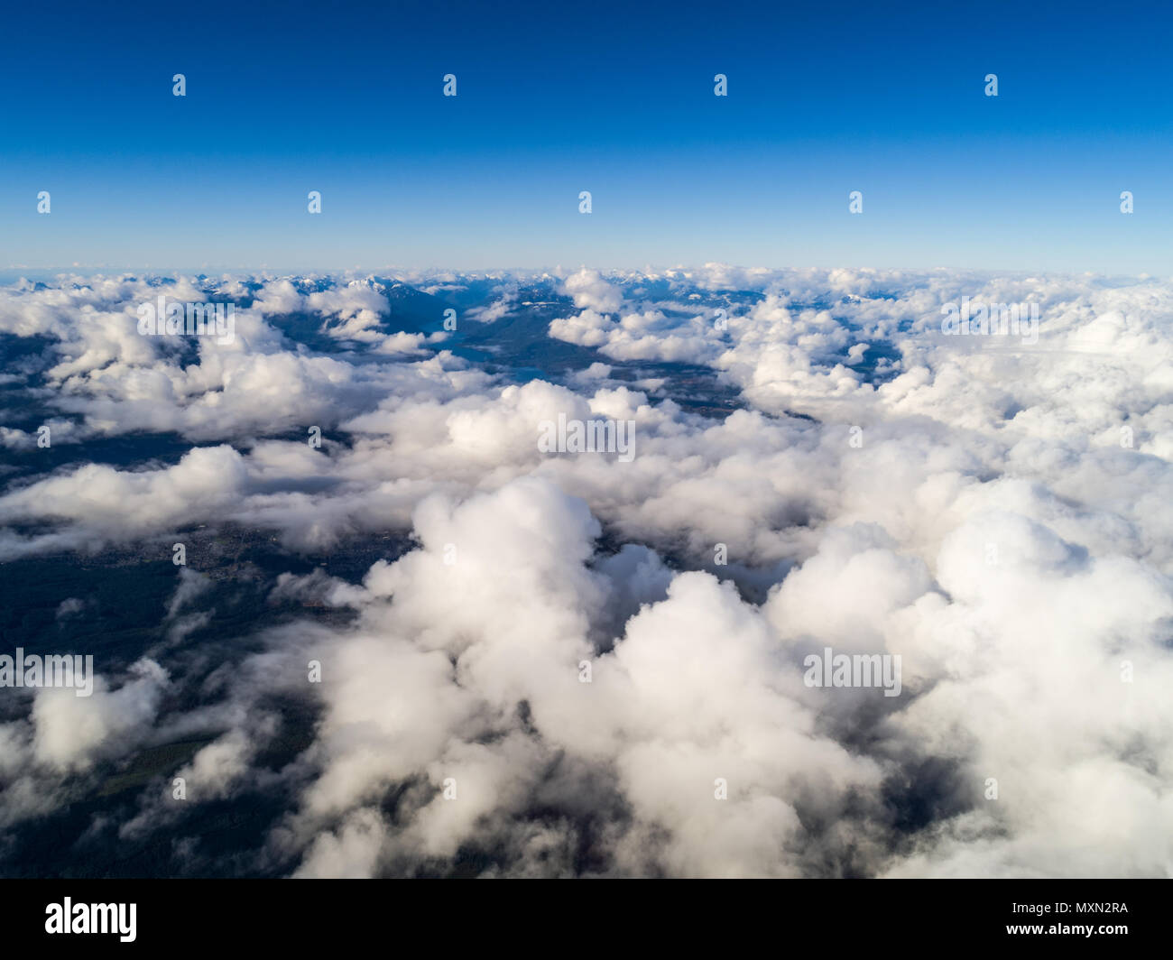 Alta altitudine shot sopra le nuvole, con le montagne sullo sfondo e un piccolo picco città fuori da sotto le nuvole Foto Stock