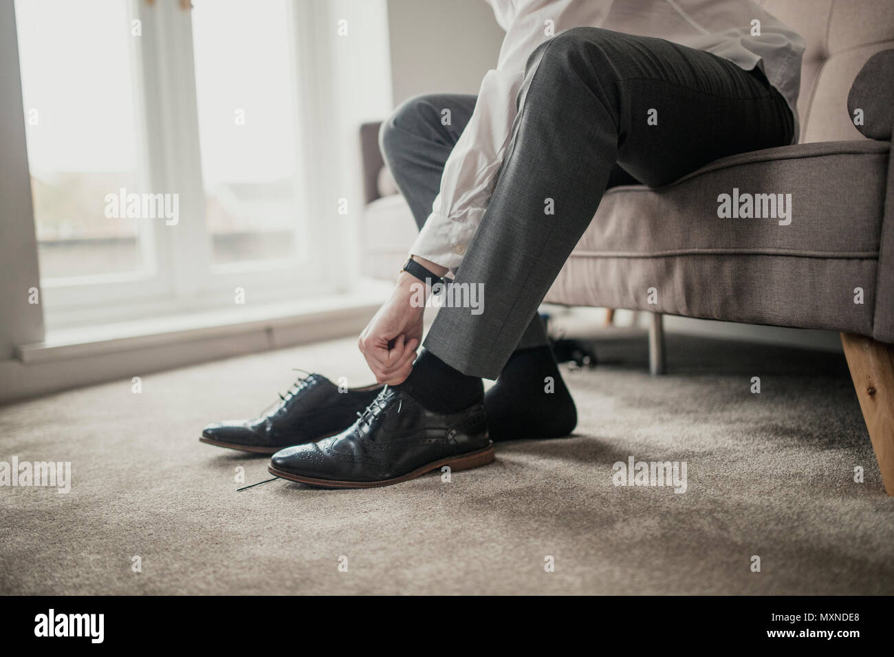Persona irriconoscibile maschio adulto seduto su un divano in un ambiente domestico il suo legatura lacci delle scarpe. Foto Stock