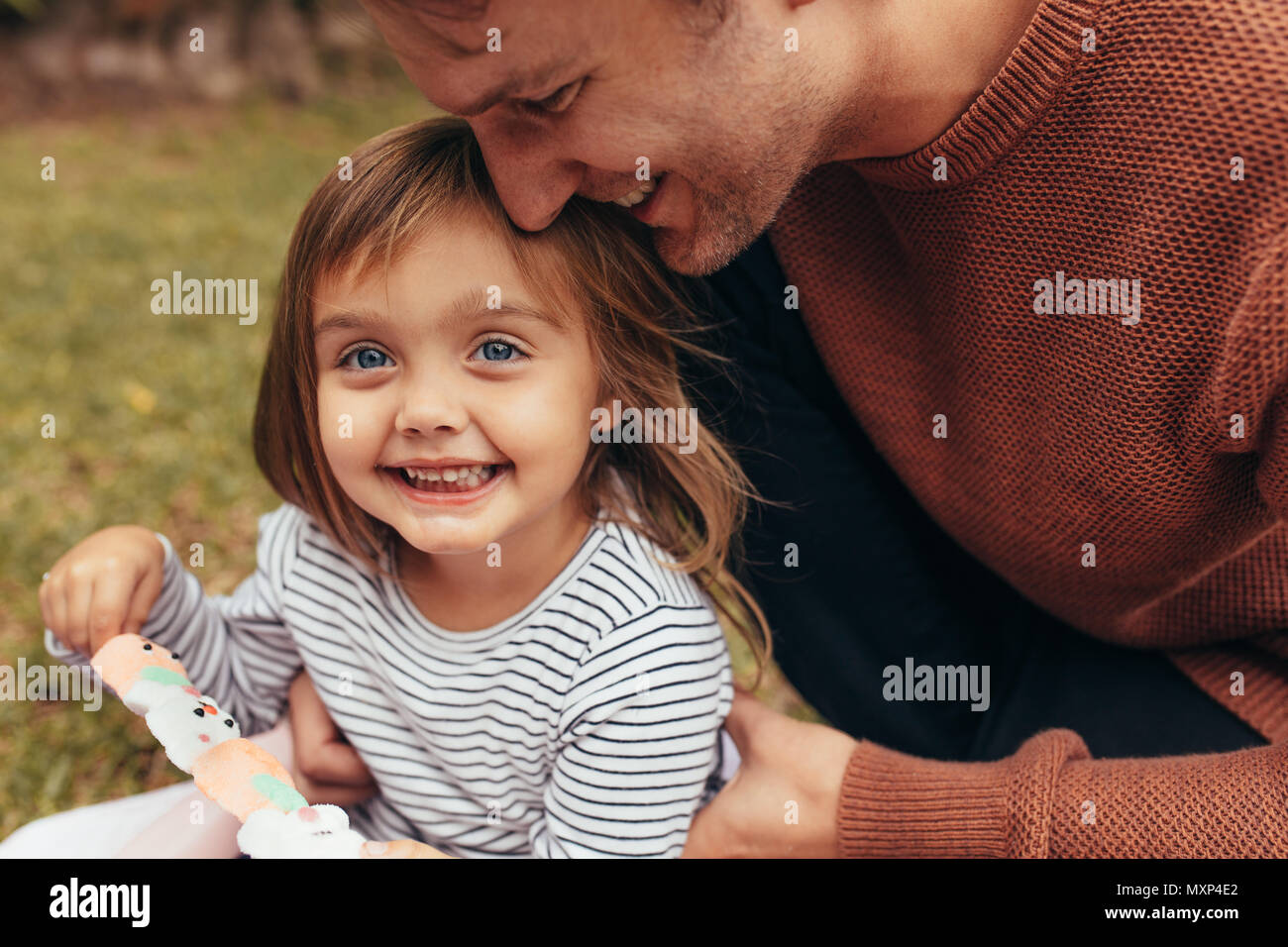 Sorridente ragazza seduta con suo padre all'aperto tenendo un zucchero candito stick. Padre e figlia di trascorrere del tempo insieme a mangiare zucchero candito. Foto Stock