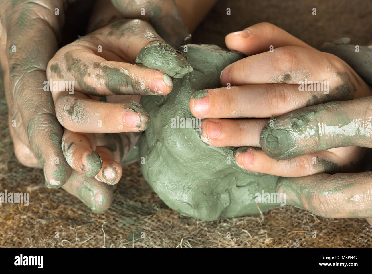 Mani di adulto aiuta il bambino a lavorare con materie prime argilla blu Foto Stock