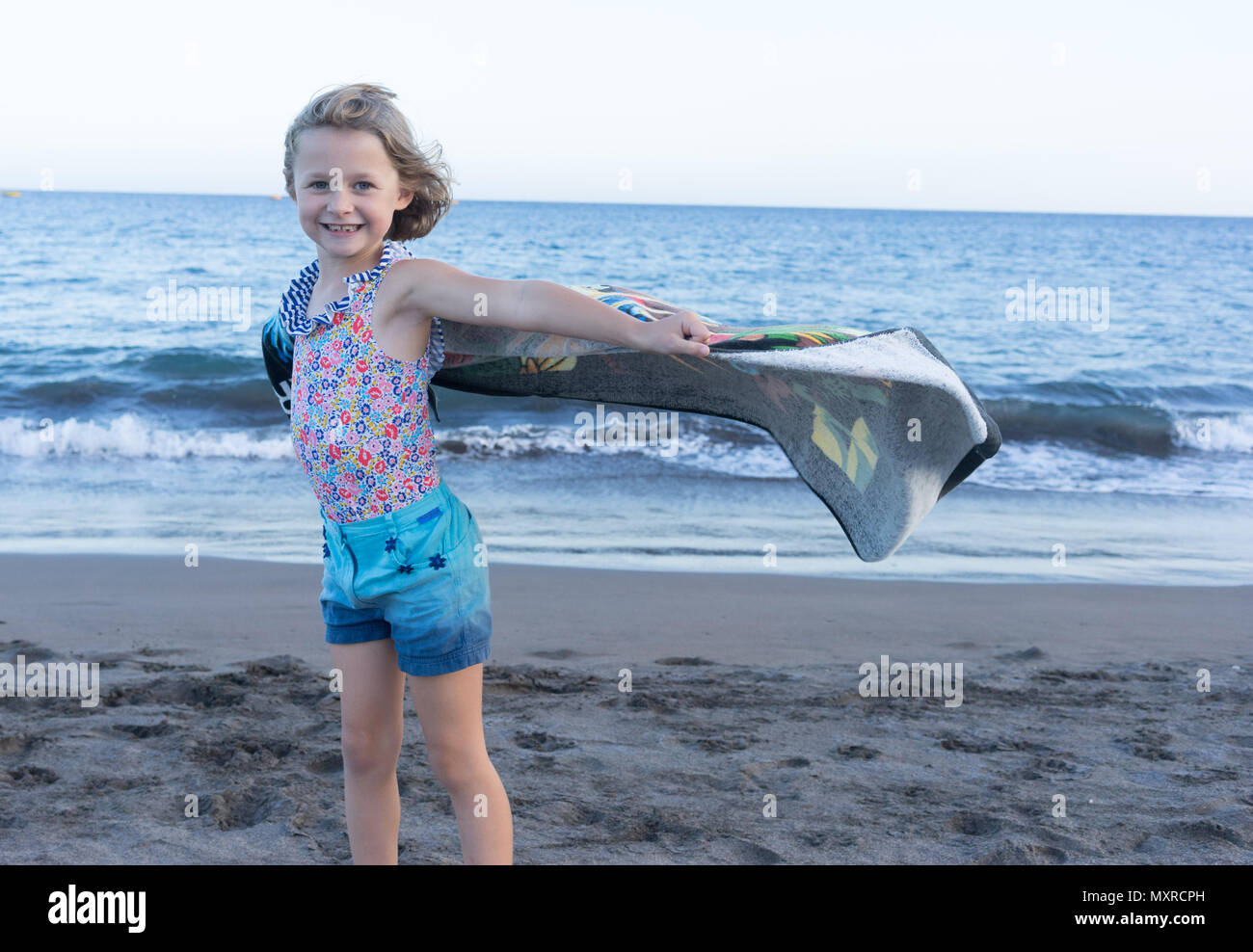 Bambino femmina sulla spiaggia tenendo un asciugamano nel vento Foto Stock