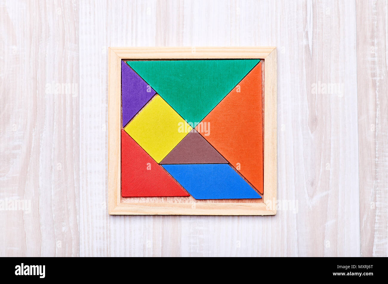 Un tangram puzzle costituito da pezzi colorati con forme geometriche, raccolti in un quadrato su una luce sullo sfondo di legno Foto Stock