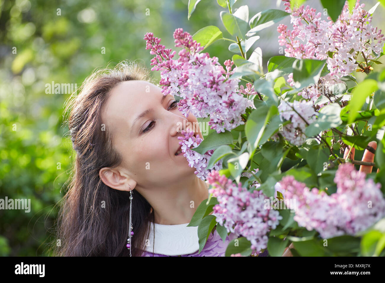 Giovane donna graziosa con bei orecchini odorare un fiore fiori lilla Foto Stock