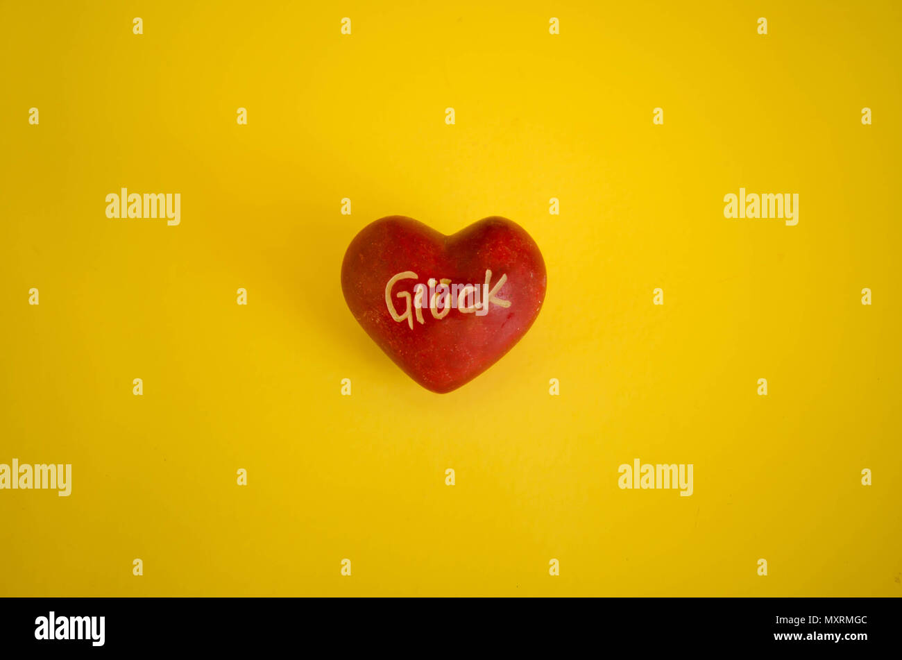 Dipinto di rosso pebble a forma di cuore su sfondo giallo. "Gluck' in tedesco, fortuna tradotto in inglese è il messaggio scritto su di esso. Foto Stock