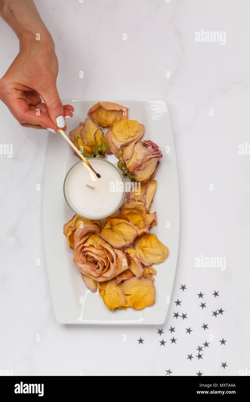 Bellissimo appartamento bianco coricato con una candela ed essiccato petali di rosa. Vista superiore, sfondo bianco piatto concetto laici Foto Stock