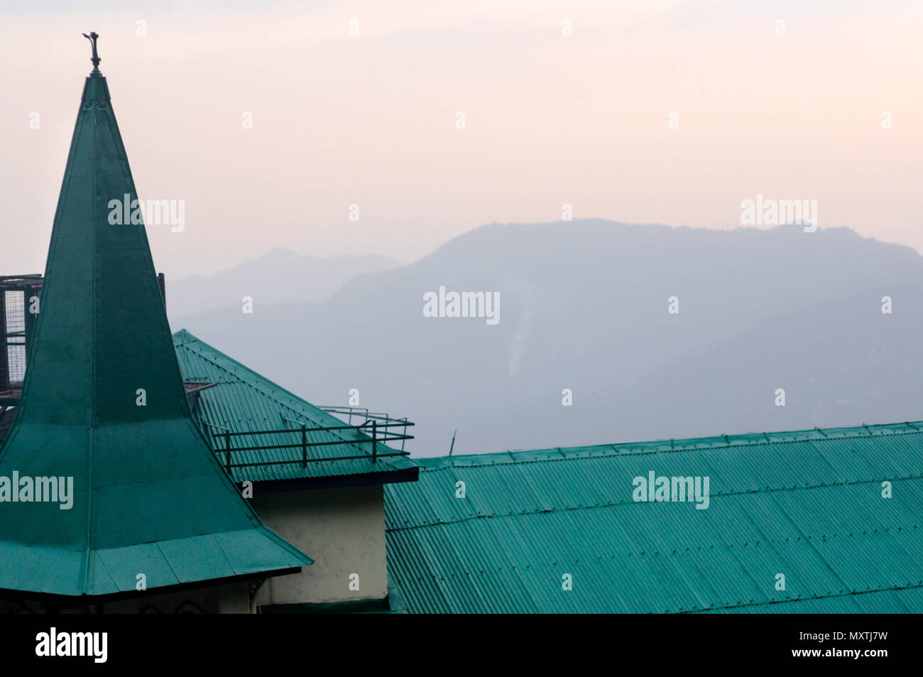 Il tetto verde e torre di una casa di campagna contro le colline blu e rosa cielo di uno splendido tramonto . Girato in shimla si mette in mostra la bellezza del luogo Foto Stock