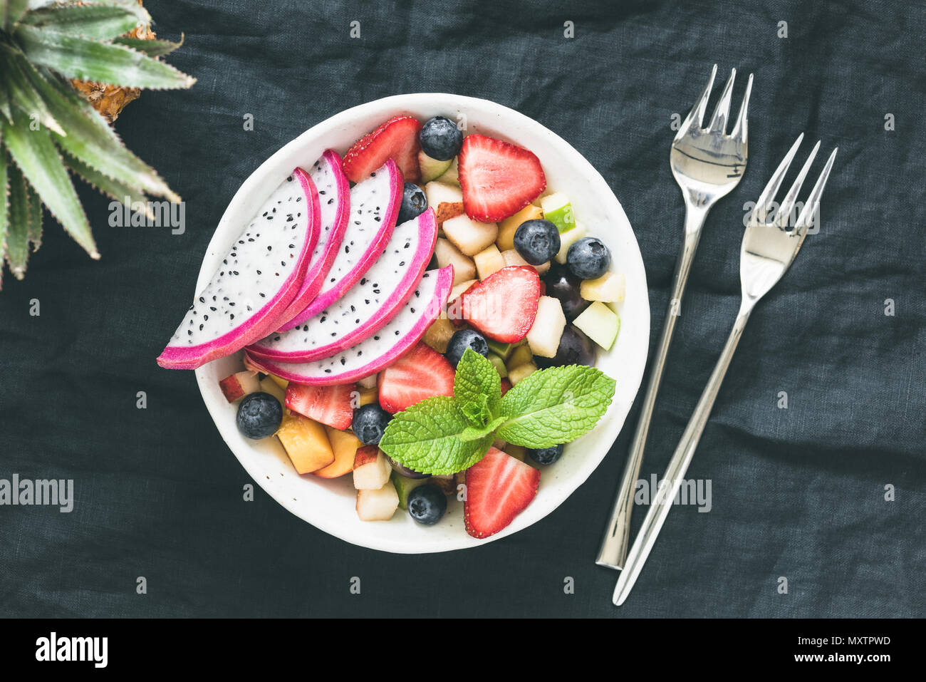 Una insalata di frutta tropicale con dragon frutto in una ciotola su sfondo scuro, tonica immagine. Tabella vista dall'alto di una sana vegano insalata di frutta Foto Stock