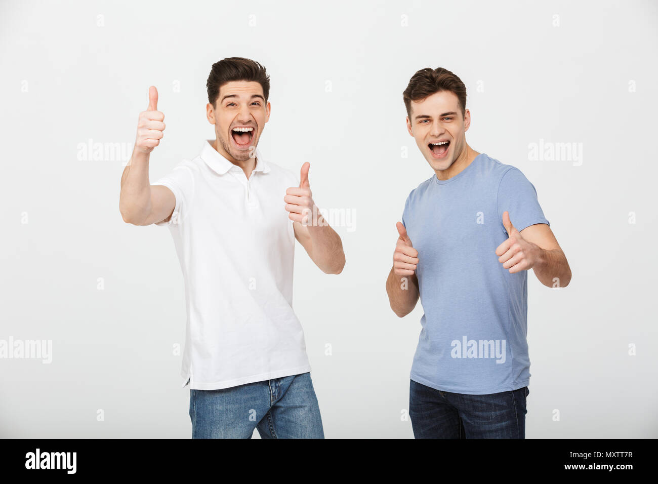 Due amici felice 30s indossando t-shirt casual e jeans sorridente e mostrando pollice in alto sulla fotocamera isolate su sfondo bianco Foto Stock