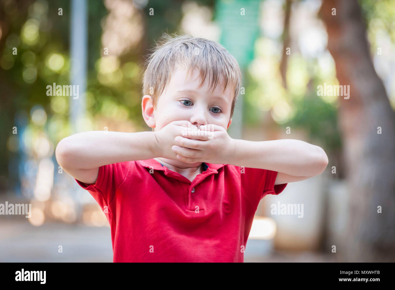 Poco serio ragazzo caucasico chiudendo la bocca con le mani. Immagine illustrativa per trauma infantile concetto, bambino traumatica esperienza. Psicologici Foto Stock