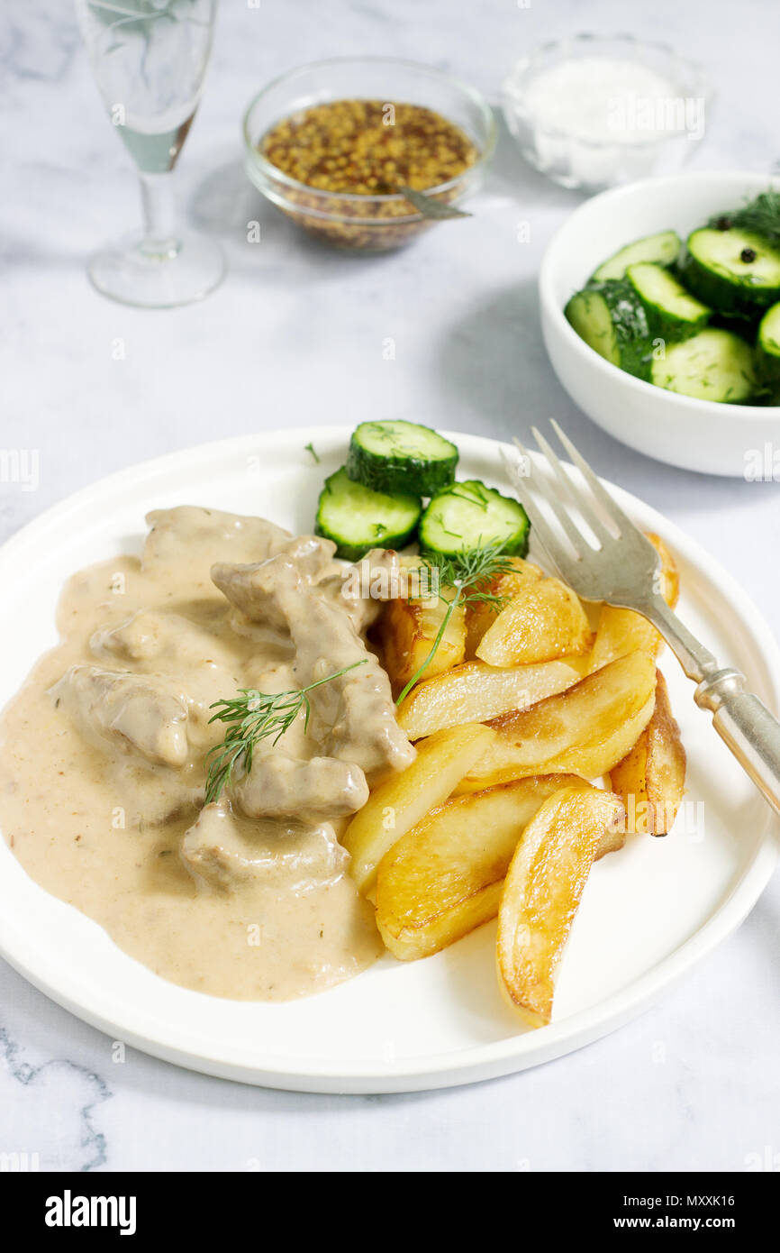 Carni bovine Stroganoff - un tradizionale russo piatto di carni bovine in panna acida salsa, servito con patate fritte, conserve di cetrioli e la vodka. Messa a fuoco selettiva. Foto Stock
