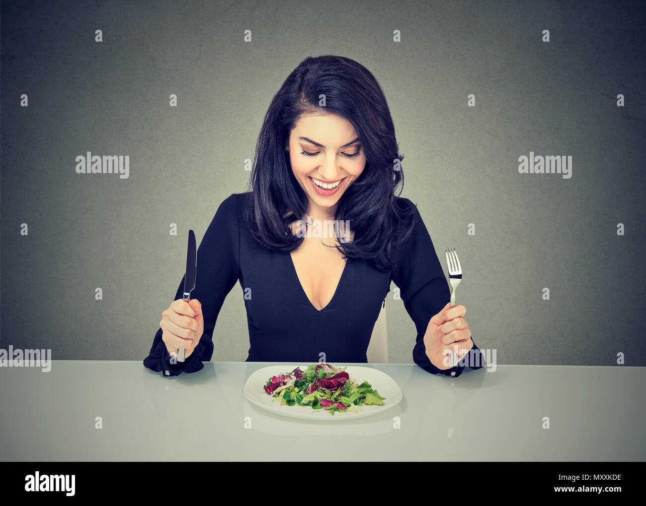 Bella bruna seduta a tavola e guardando eccitato in corrispondenza della piastra con insalata avente una dieta salutare per la perdita di peso Foto Stock