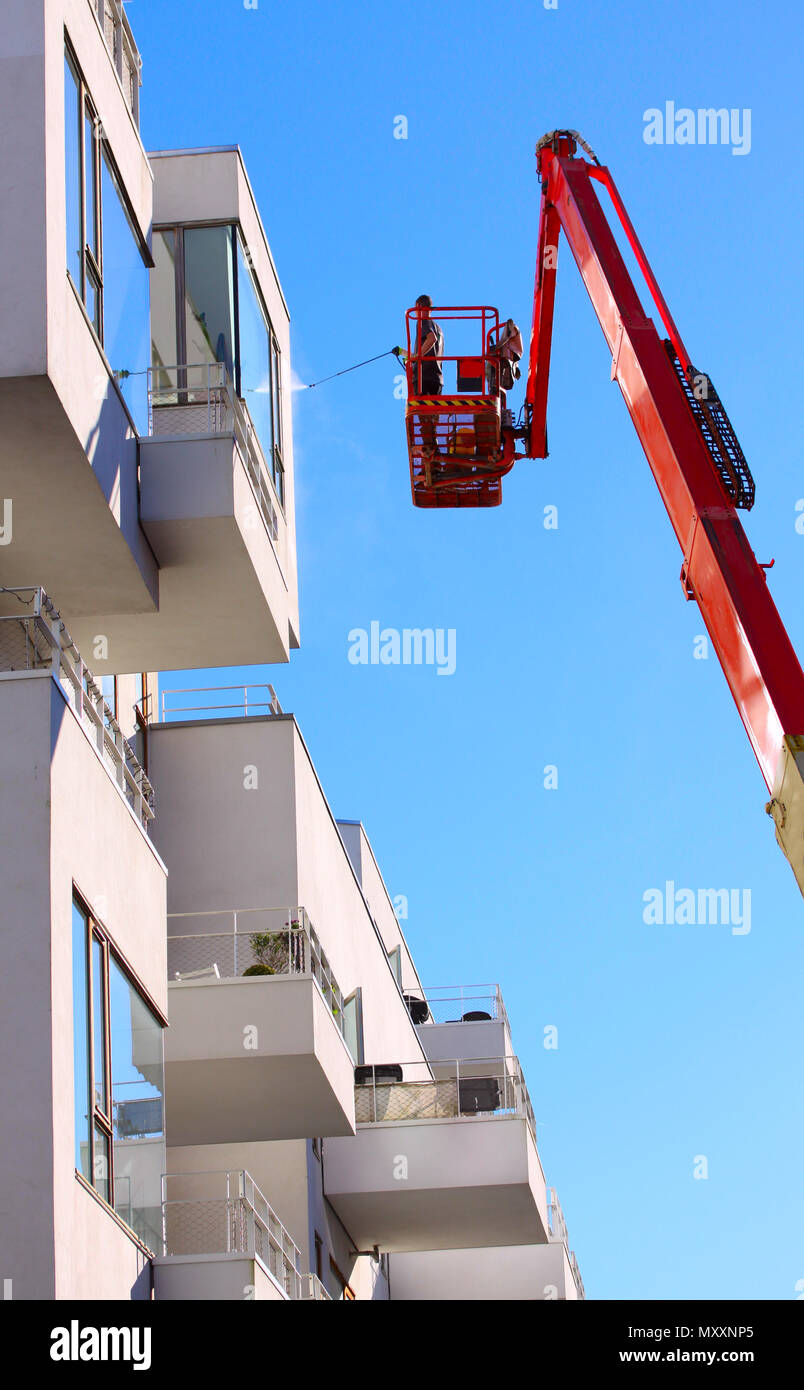 Uomo facciata di pulizia di un moderno stile minimalista appartamento edificio su un braccio telescopico elevatore utilizzando la pressione di lavaggio a getto con cielo blu sullo sfondo Foto Stock