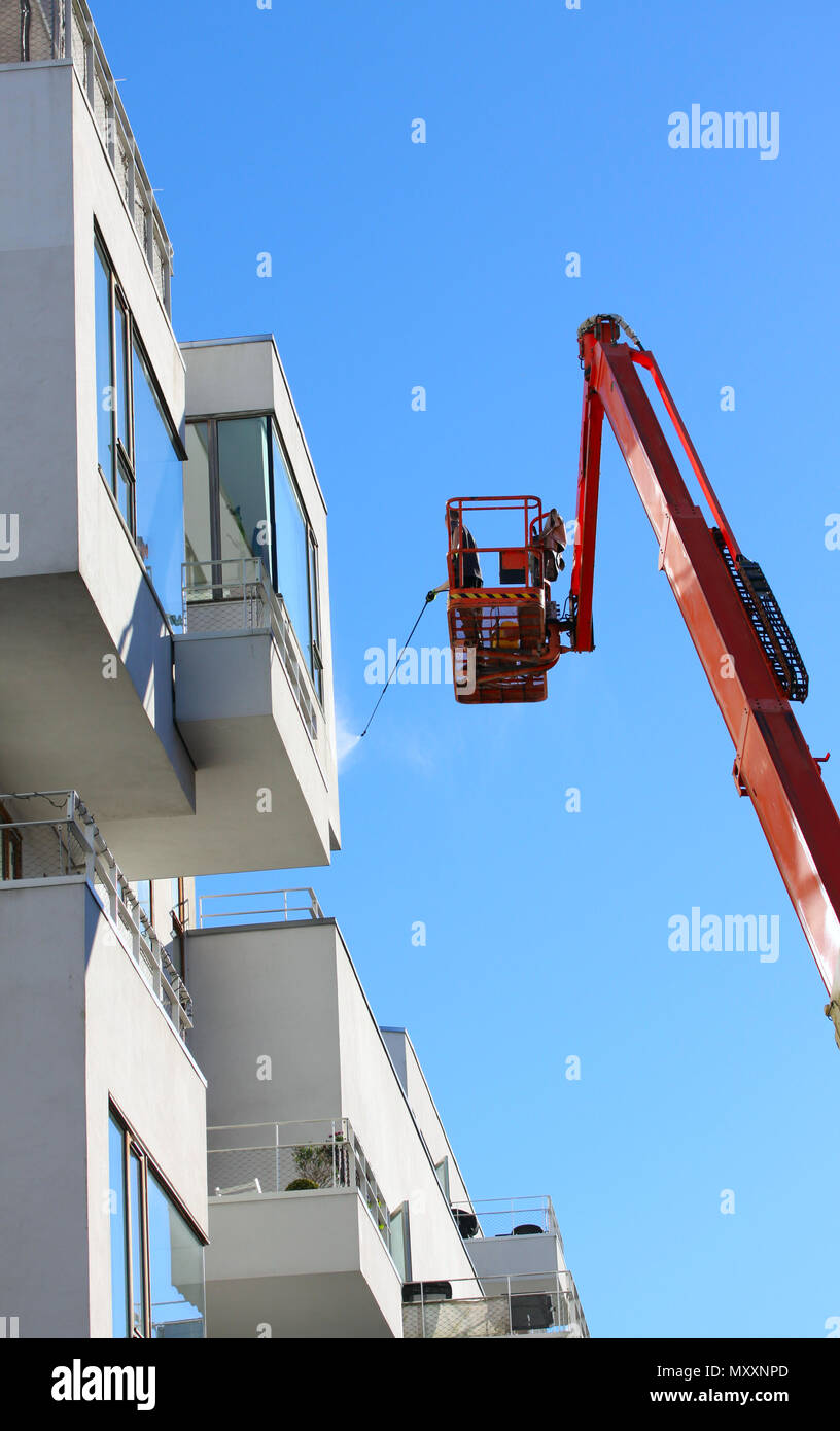 Uomo facciata di pulizia di un moderno stile minimalista appartamento edificio su un braccio telescopico elevatore utilizzando la pressione di lavaggio a getto con cielo blu sullo sfondo Foto Stock