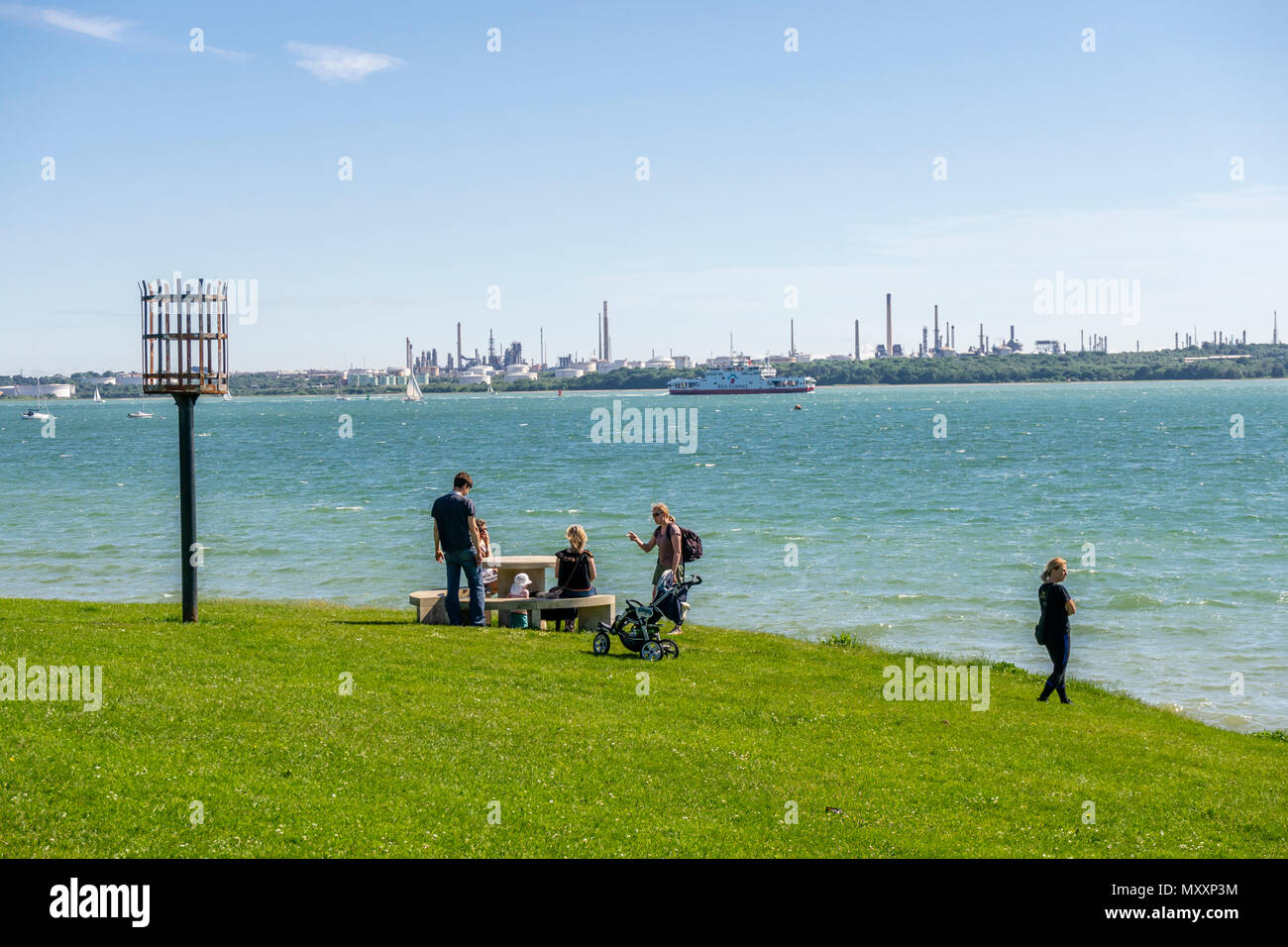 Persone che godono il sole a Netley Beach lungo Southampton acqua con la raffineria Fawley in background 2018 maggio, Netley, Hampshire, Inghilterra, Regno Unito Foto Stock