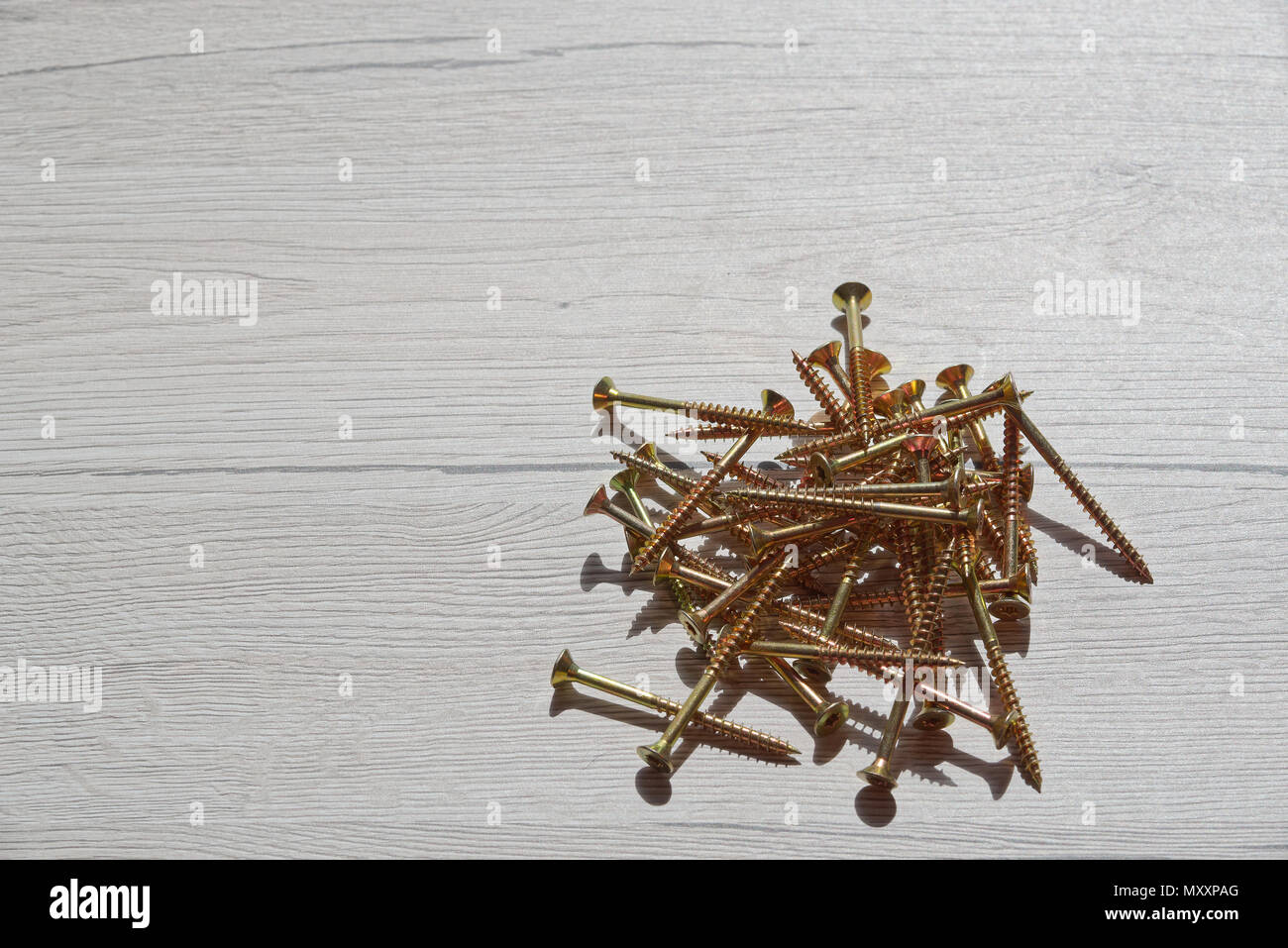 Pila di giallo lucido viti sul grigio Sfondo di legno Foto Stock