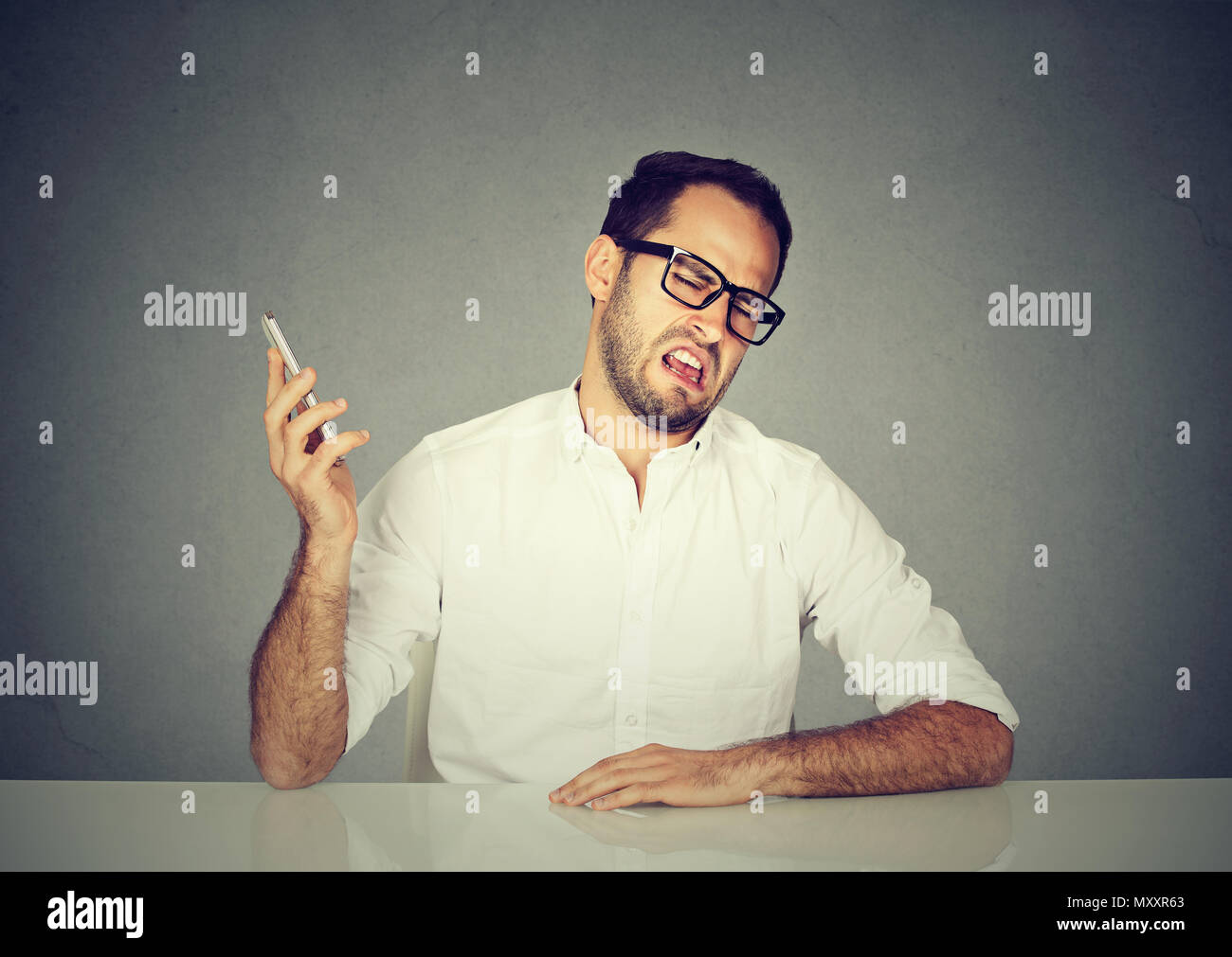 Uomo in camicia bianca e occhiali smorfie e ignorando il partner di conversazione mentre avente chiamata telefonica Foto Stock