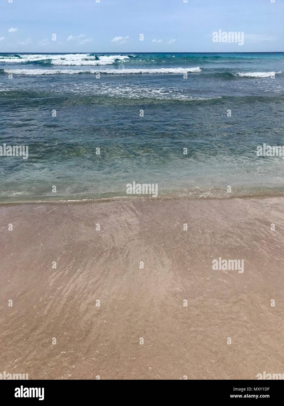 Idilliaco e bel pomeriggio in spiaggia in Barbados (isola dei Caraibi): Nessuno, di sabbia bianca e limpide acque turchesi con le onde e una soleggiata cielo blu Foto Stock