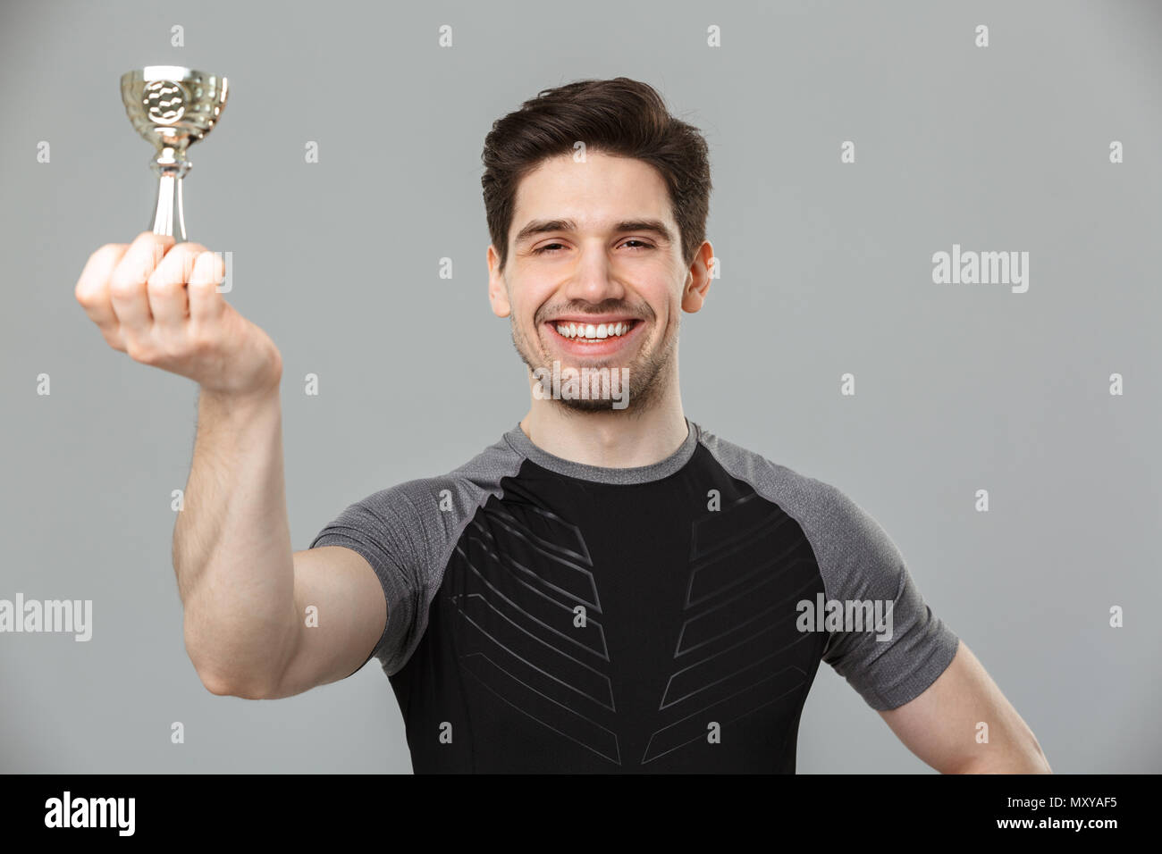 Immagine di felice giovane atleta standing isolate su muro grigio Sfondo tenendo award. Foto Stock