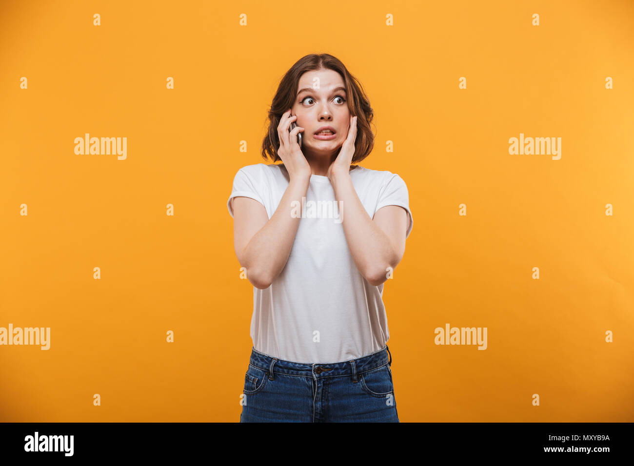 Immagine del sistema nervoso giovane donna in piedi isolato su sfondo giallo parla al telefono cellulare. Guardando a parte Foto Stock