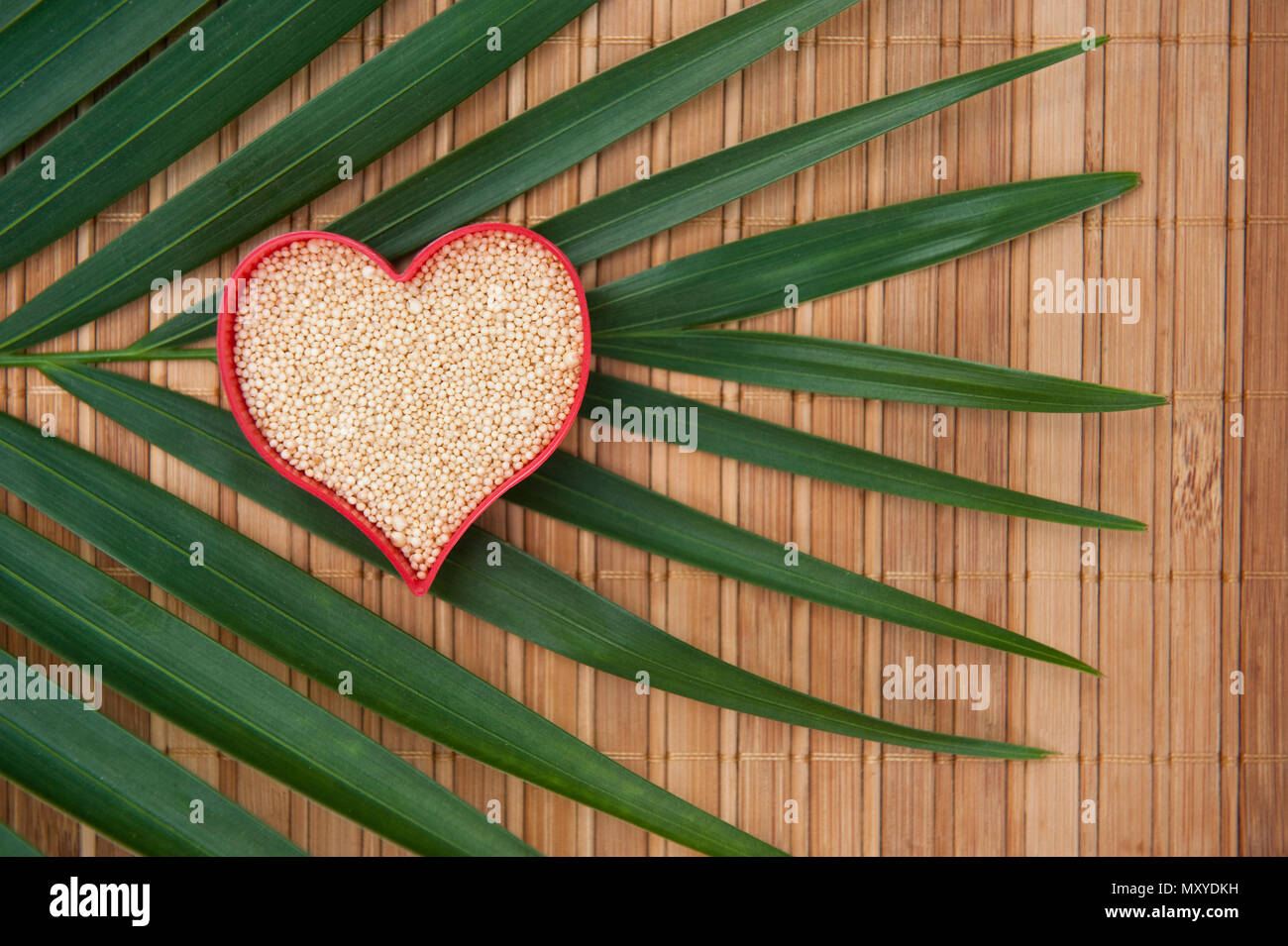 Cuore colmo di amaranto su un tappetino di bambù con un ramo di palma Foto Stock