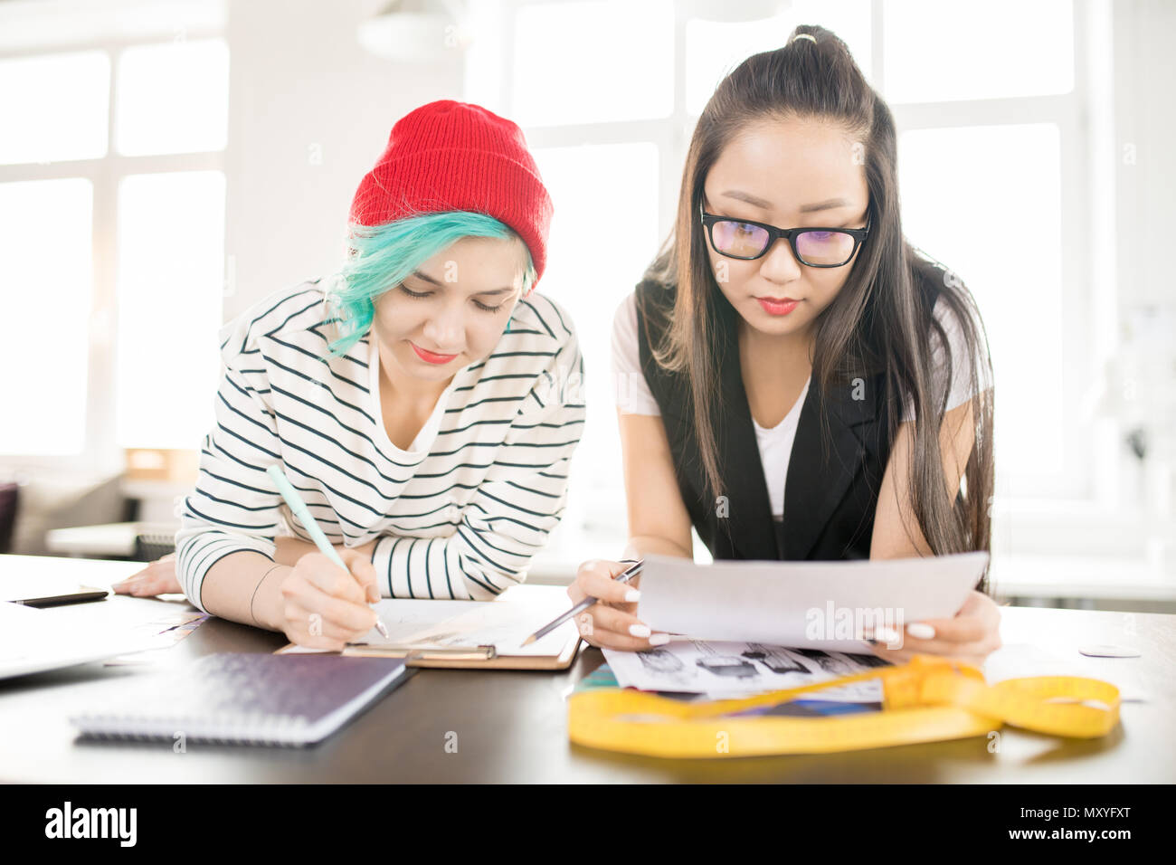 Ritratto di due giovani creativi delle donne che lavorano in fashion design schizzi di disegno e di collaborare sui progetti in piedi da sarti tabella nella moderna ateli Foto Stock