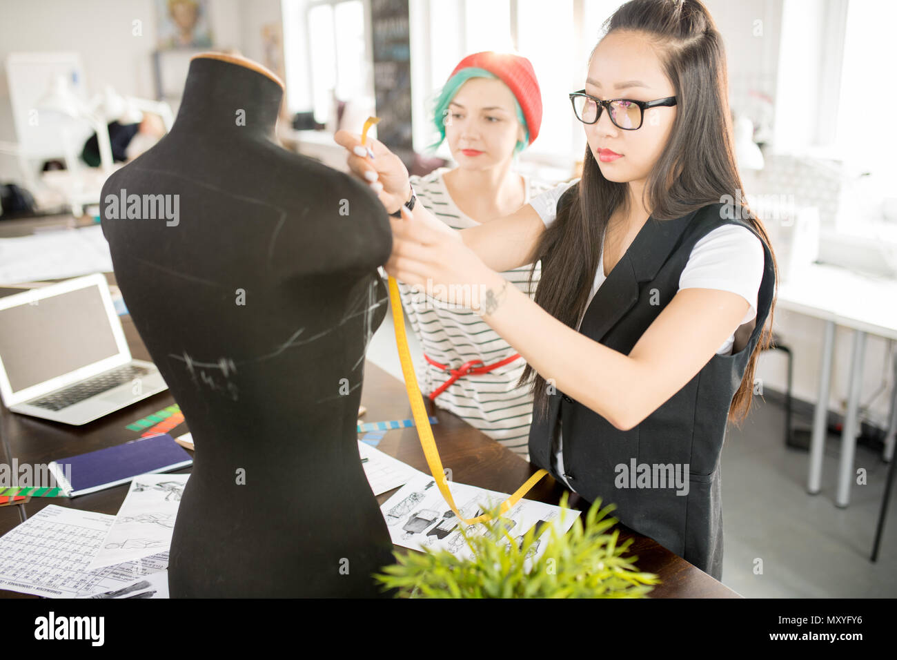 Vita ritratto di due contemporary fashion designer che lavorano in atelier di collaborare su progetto creativo, concentrarsi sul giovane donna asiatica la misurazione se Foto Stock